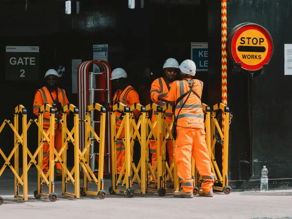 Construction workers in high-visibility gear meeting at site entrance.