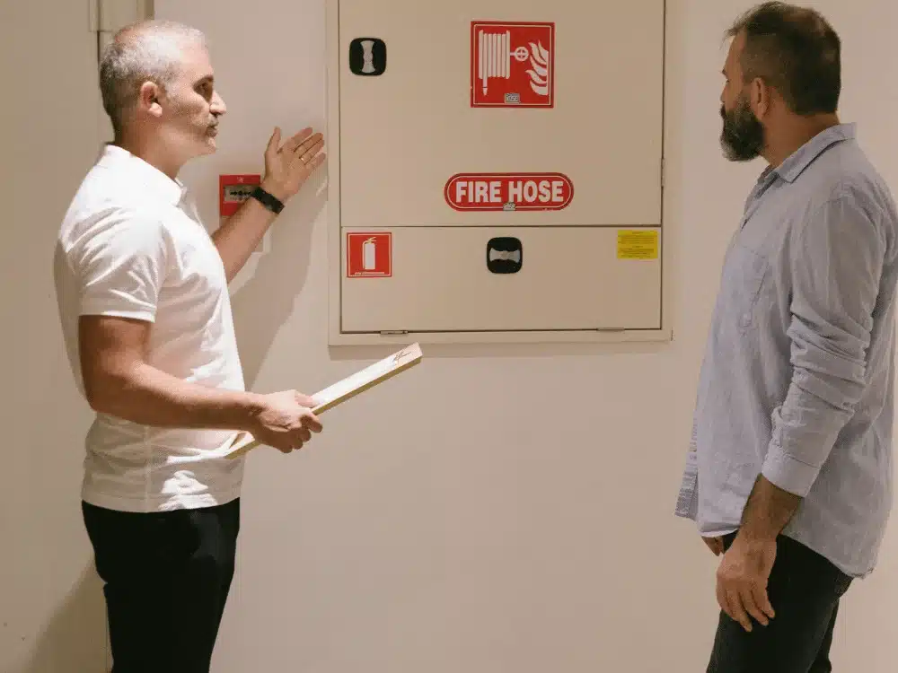 Fire safety officers examining a wall-mounted red fire hose cabinet in a building.
