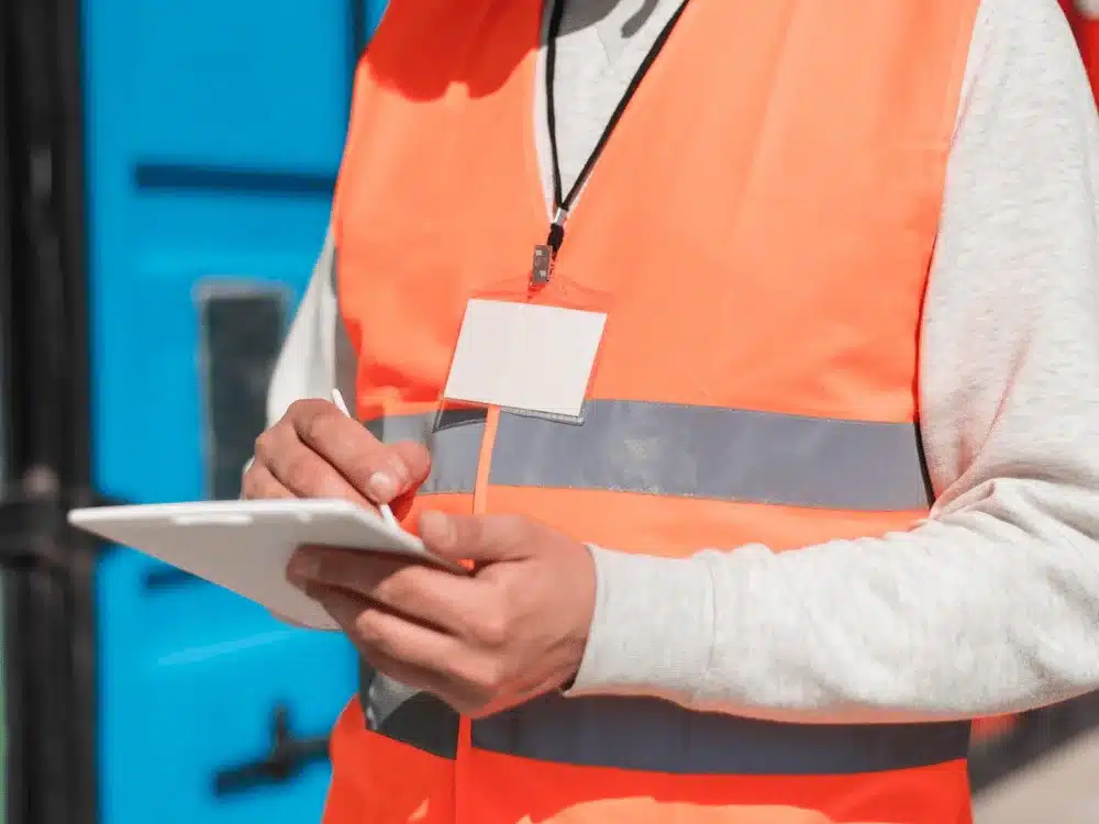 Construction worker in a neon orange safety vest making notes on a clipboard, emphasizing safety protocols.