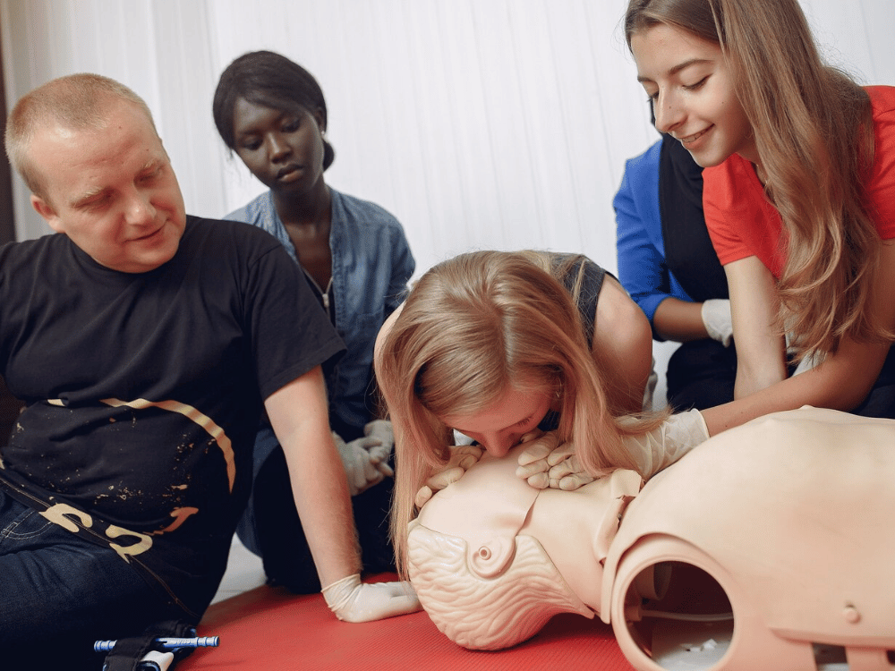 First aid trainees learning resuscitation techniques on a dummy with an instructor's guidance.