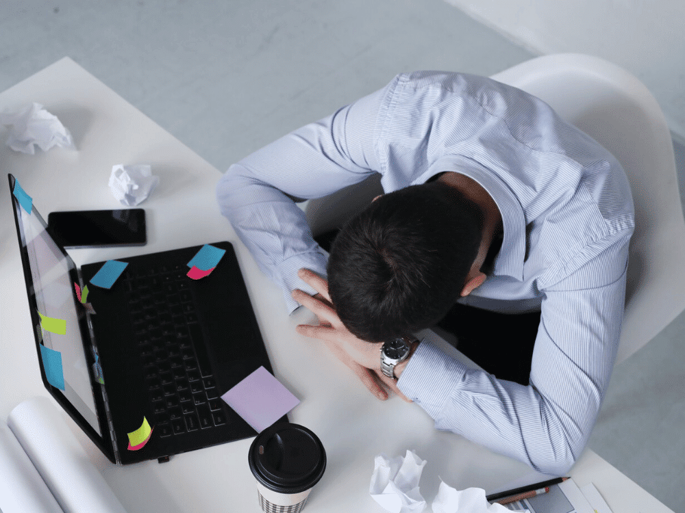 A person sitting at a desk with their head on the table.