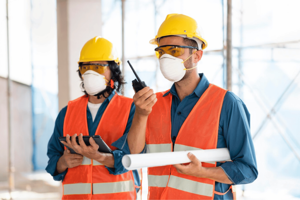 Two construction workers wearing safety gear and holding cell phones.