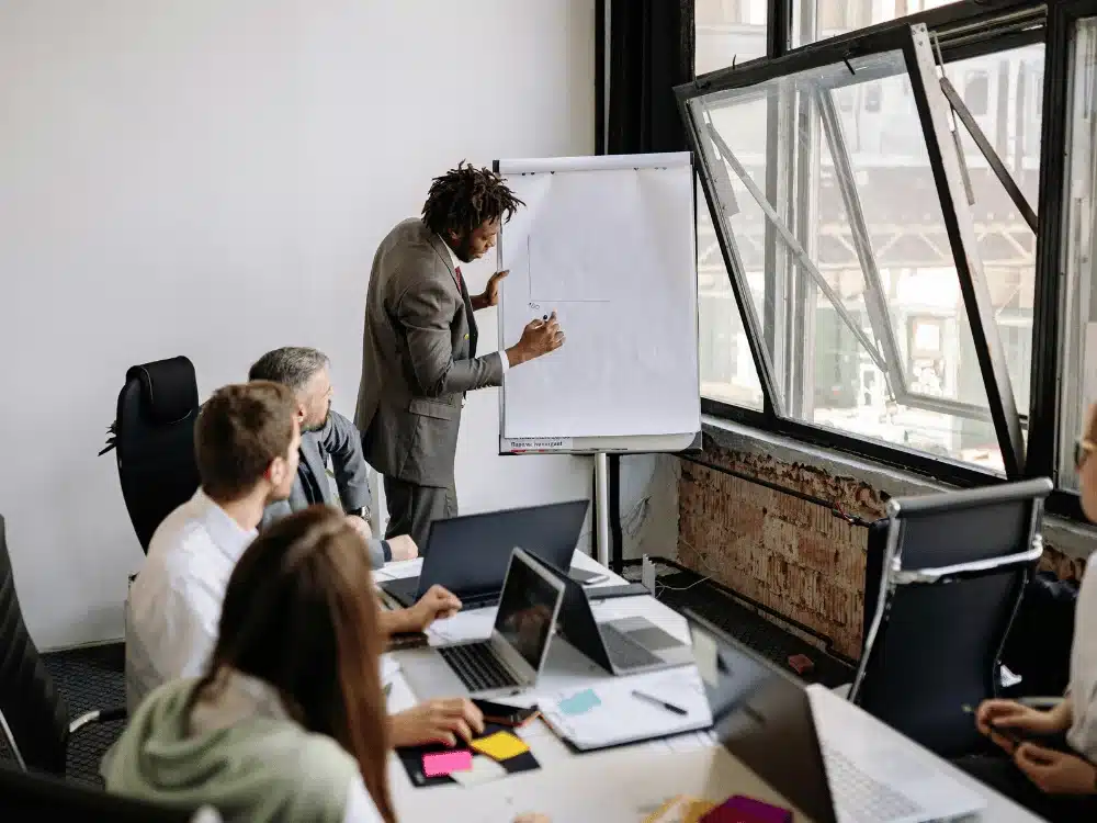 Business team attentively listening to a colleague presenting on a flip chart.