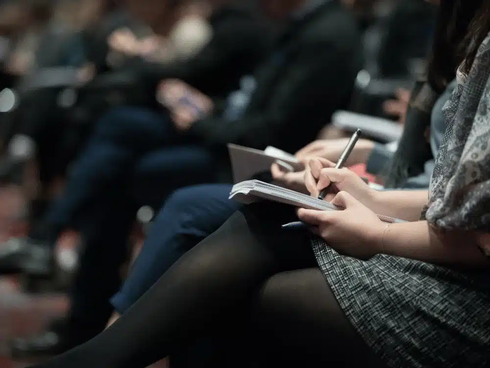 Person taking notes during a conference or seminar, focused on writing.
