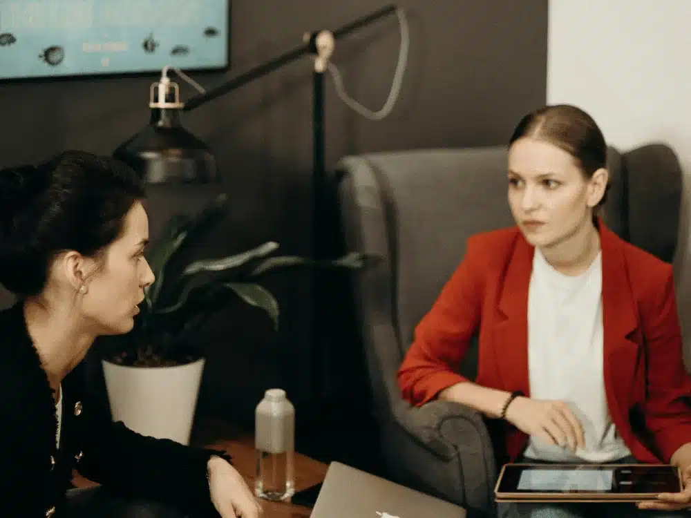 Two businesswomen engaged in a serious discussion in a modern office setting.