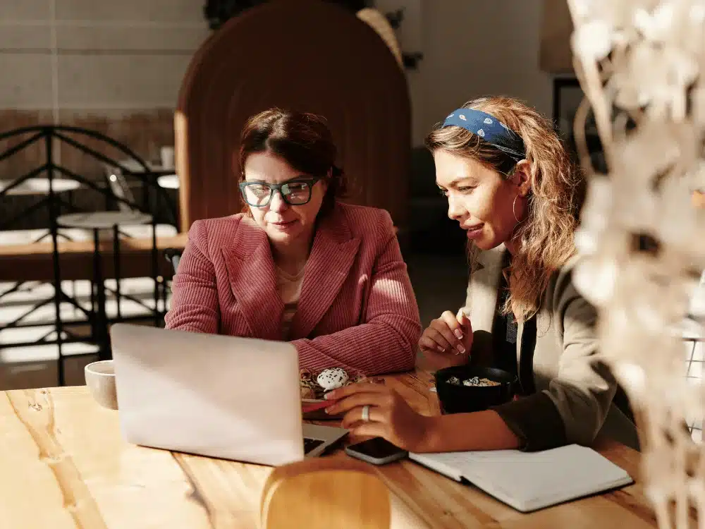 Professional meeting between two women discussing work over coffee and a laptop.
