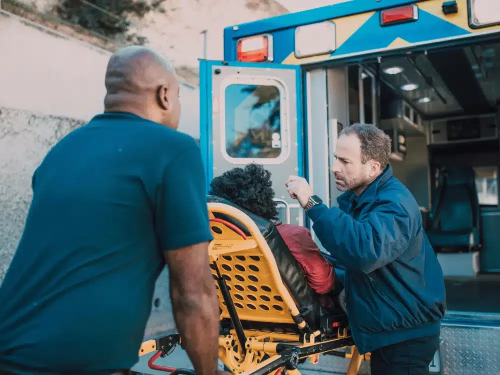 Emergency medical technicians assisting a patient into an ambulance on a stretcher.