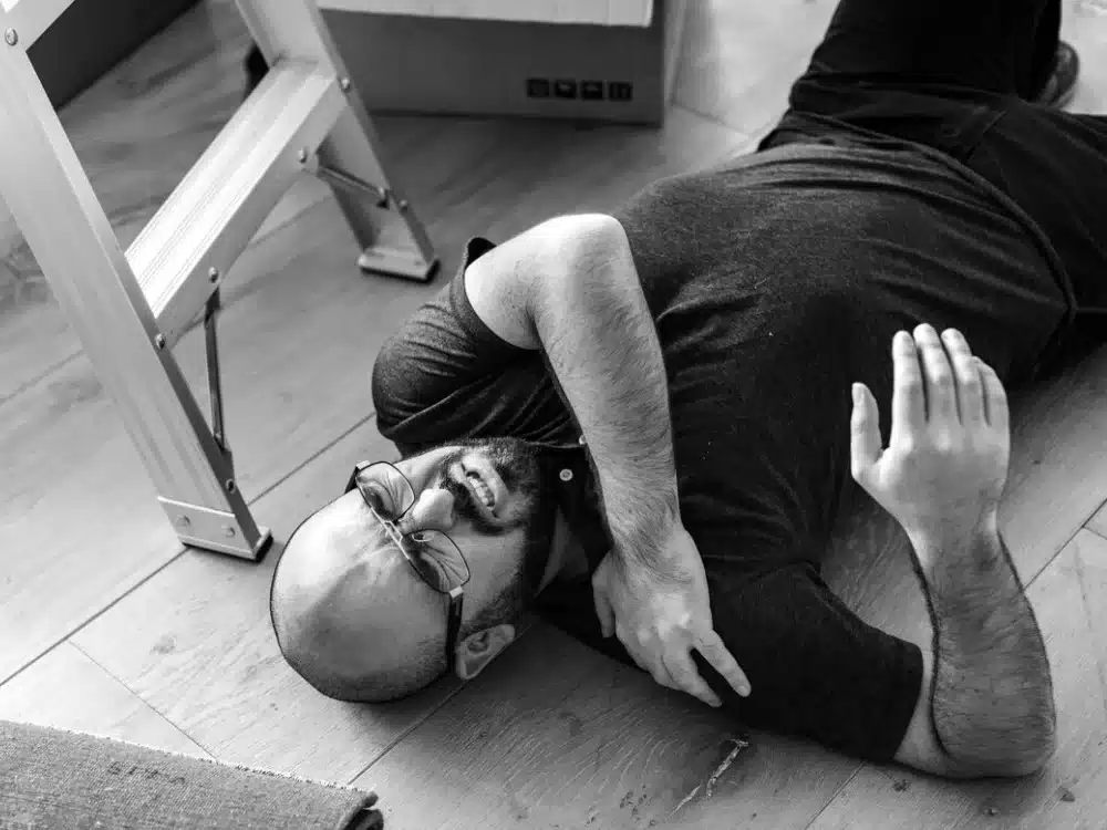 Black and white image of a man lying on the floor appearing injured next to a ladder.