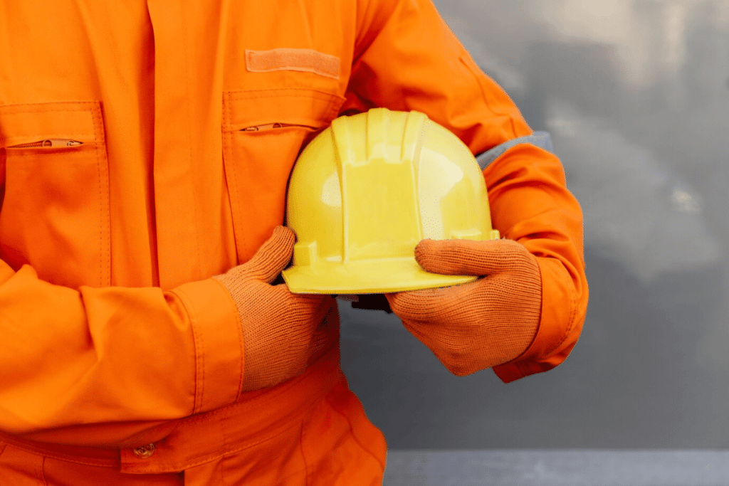A person in an orange safety suit holding a hard hat.