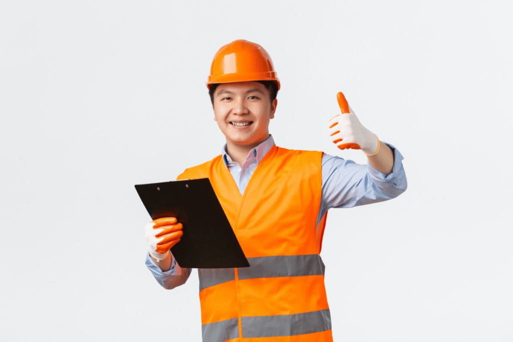 A person in an orange vest holding a clipboard and giving a thumbs up.