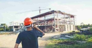 Worker with hard hat surveying construction site progress.