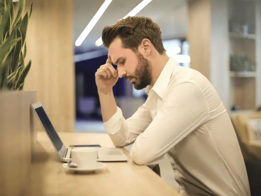 Businessman deep in thought while working on a laptop in a modern office setting.