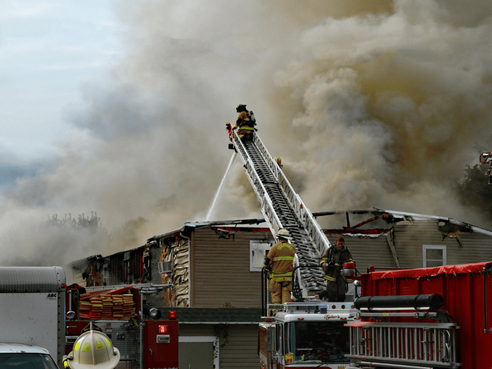 Firefighters ascend ladder amidst thick smoke to extinguish a building fire.