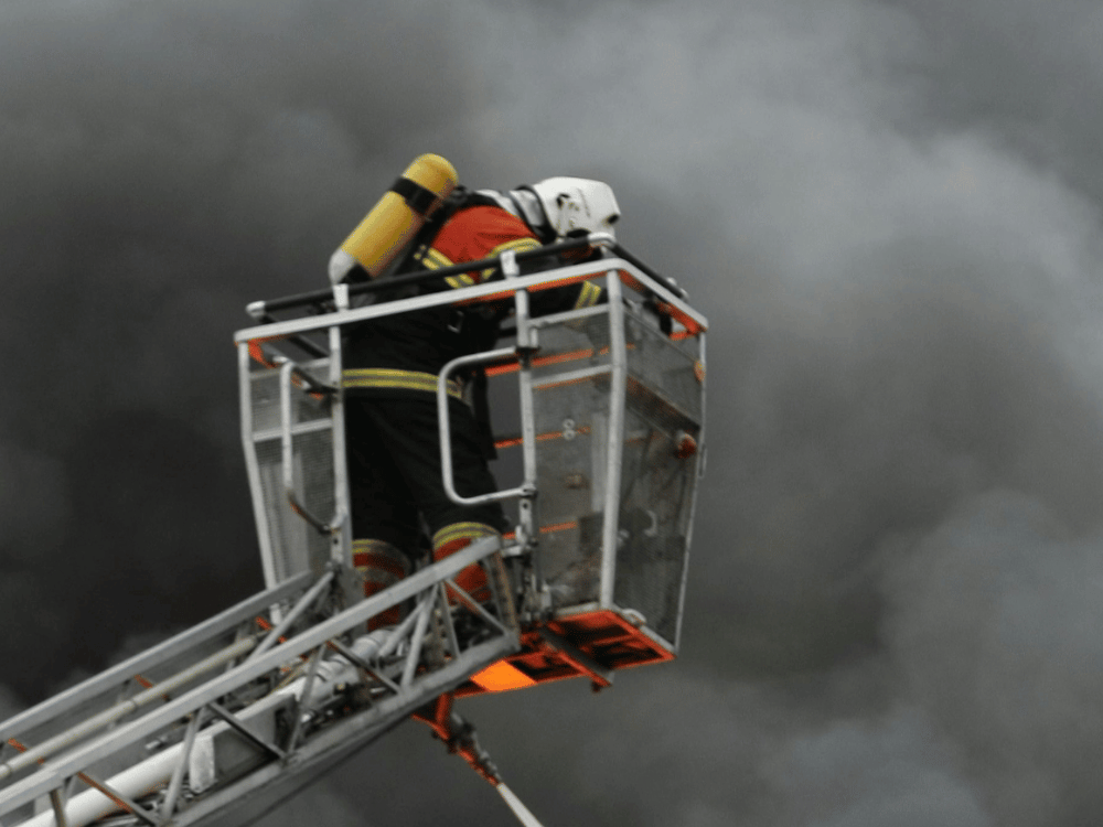 Firefighter in aerial platform amidst dense smoke during firefighting efforts.