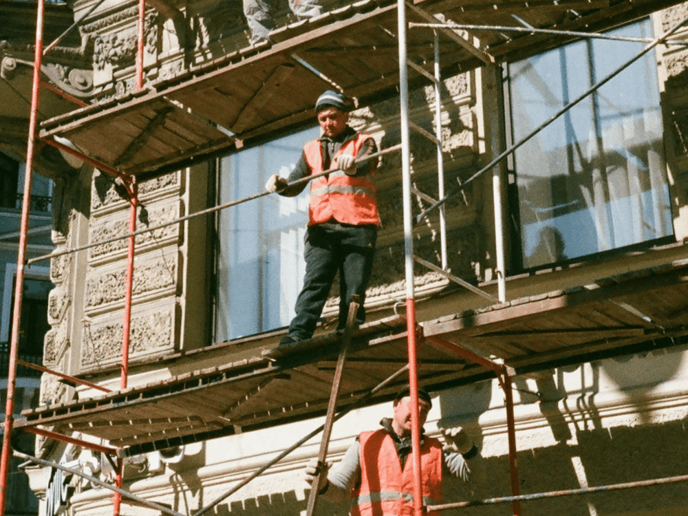 Construction workers on scaffolding against a historic building.
