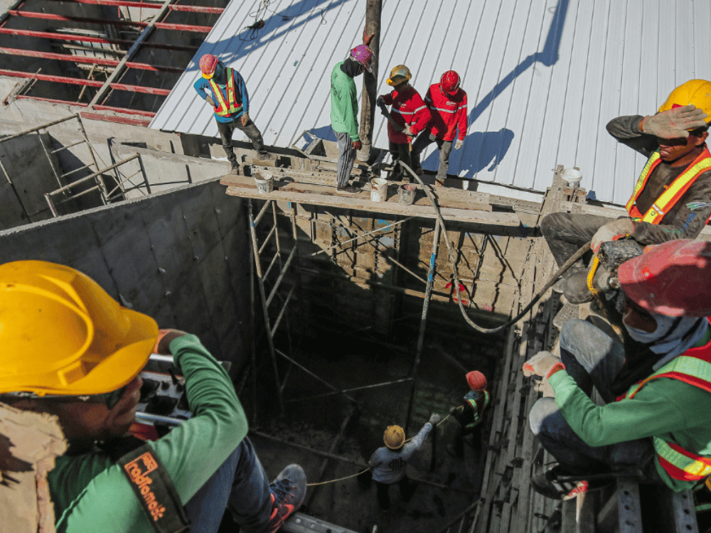 A group of construction workers wearing safety vests and helmets working on a concrete formwork at a building site.