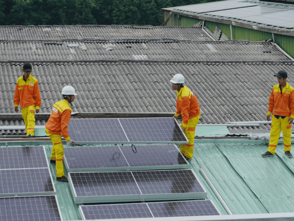 A team of workers in high-visibility orange gear installing solar panels on a grey tiled roof.