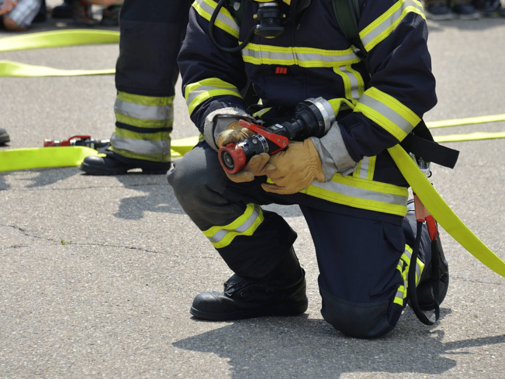 Firefighter crouched on pavement securing a hose coupling.