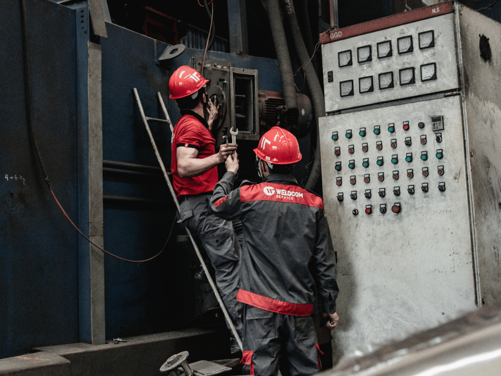 Technicians in red helmets working on industrial machine maintenance.
