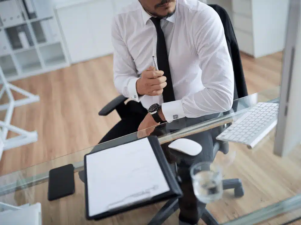 Pensive businessman with pen in hand and paperwork at office desk.