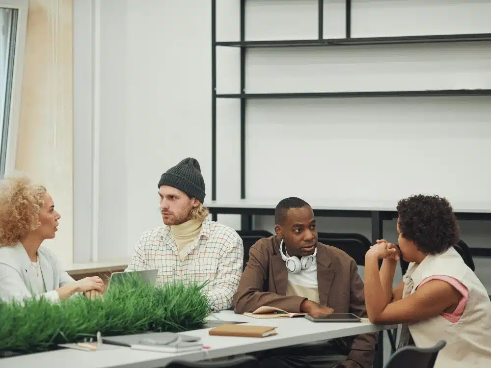 Group of diverse professionals brainstorming ideas in a modern office setting with plants and notebooks.