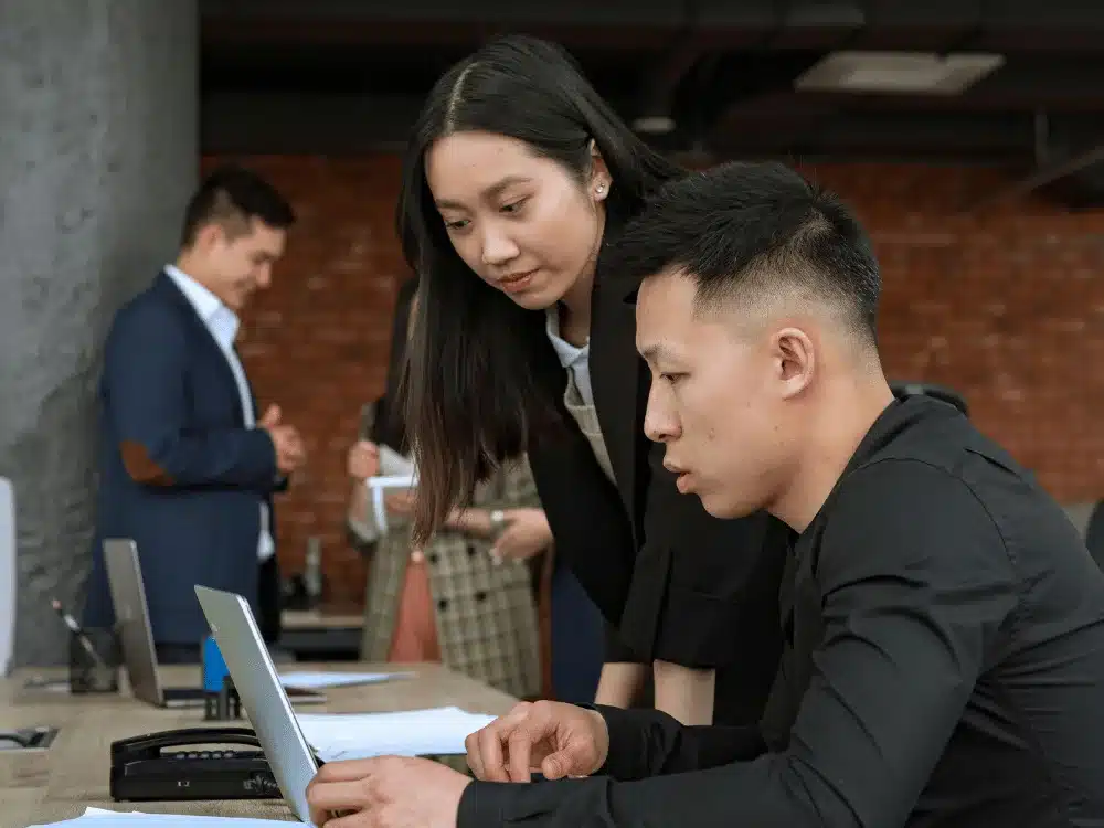 Two colleagues collaborating on a laptop in a modern office setting.