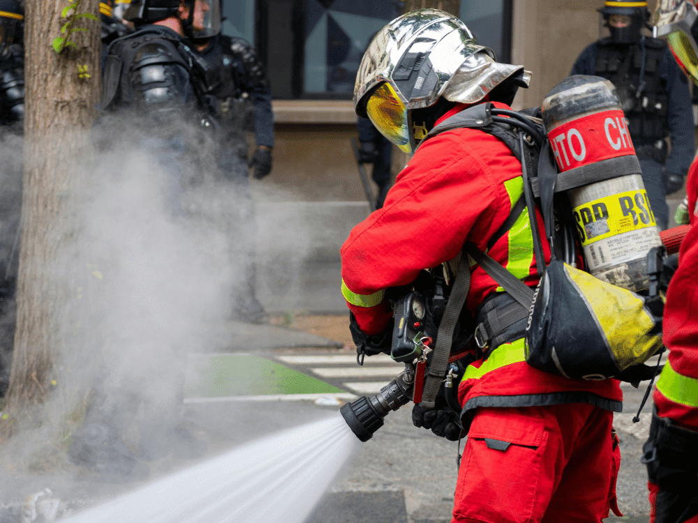Fireman in protective gear using water jet to douse urban fire.
