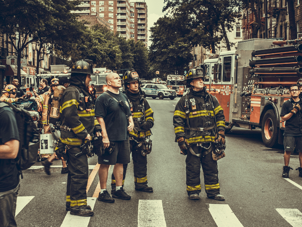 Firefighters in gear standing by firetruck on an urban road after an incident.
