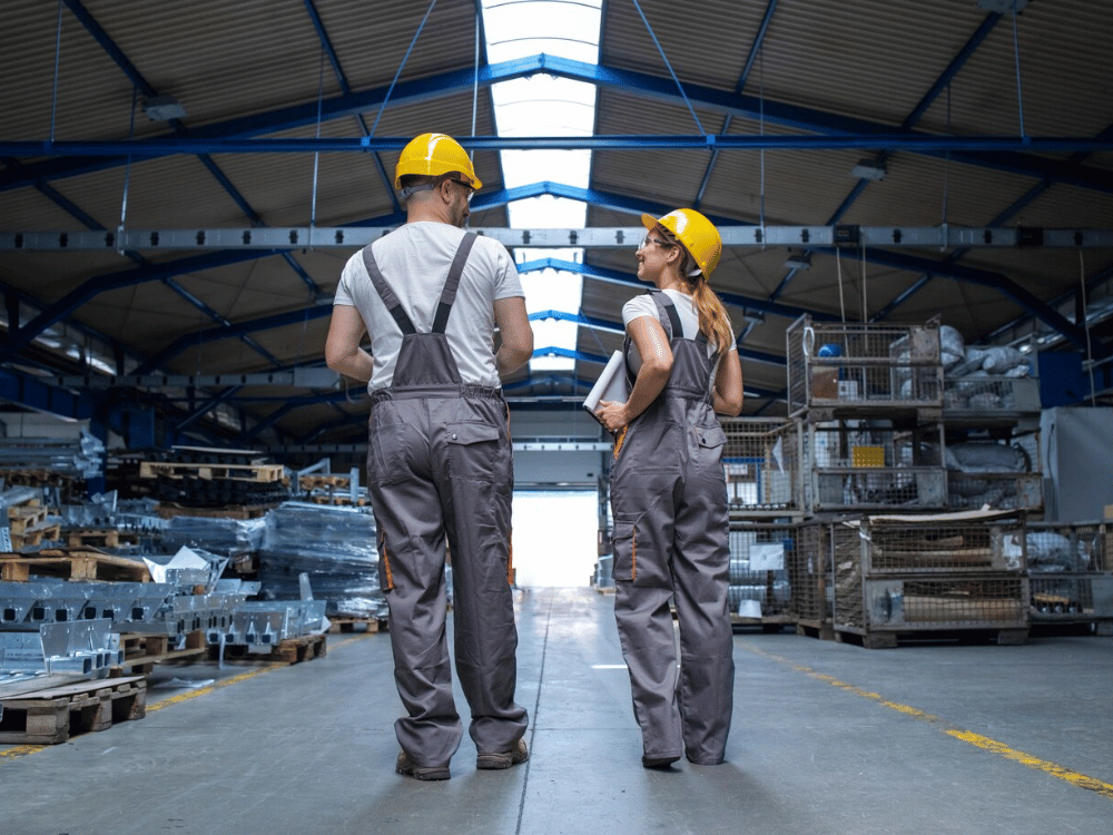 Two individuals in overalls standing in a warehouse.