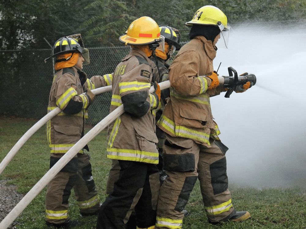 Firefighters in protective gear using a hose to extinguish a fire.