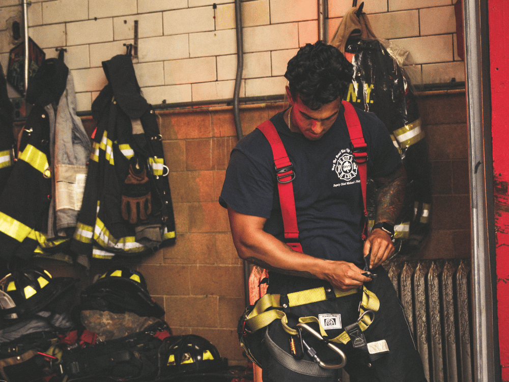 Fireman securing harness amid firefighting equipment.