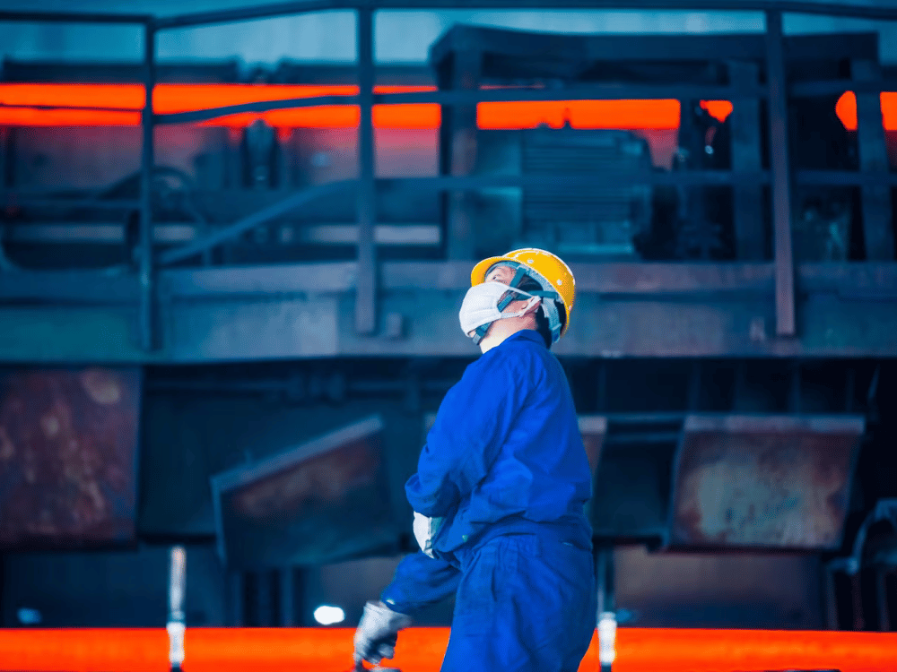 A worker is standing in front of a steel mill.