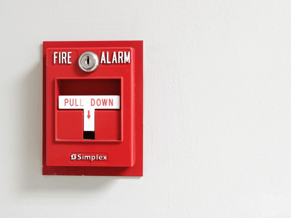 A red fire alarm mounted on a white wall.