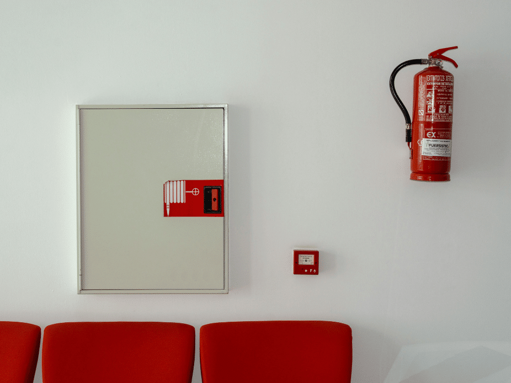 A fire extinguisher mounted on the wall next to two red chairs.