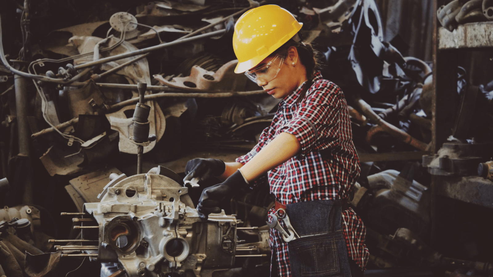 A woman in a hard hat working on an engine.