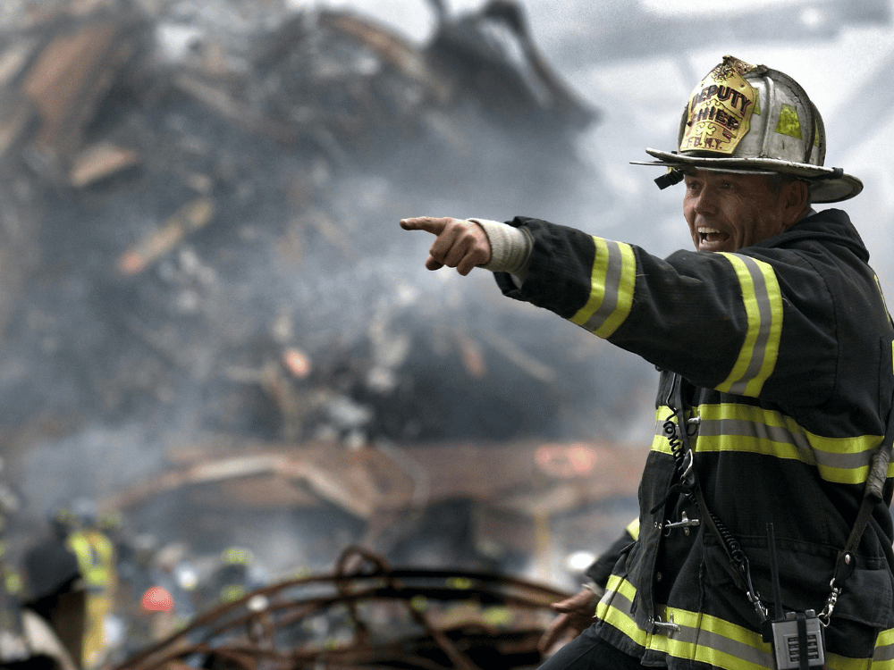 A firefighter pointing at something in the middle of a pile of rubble.