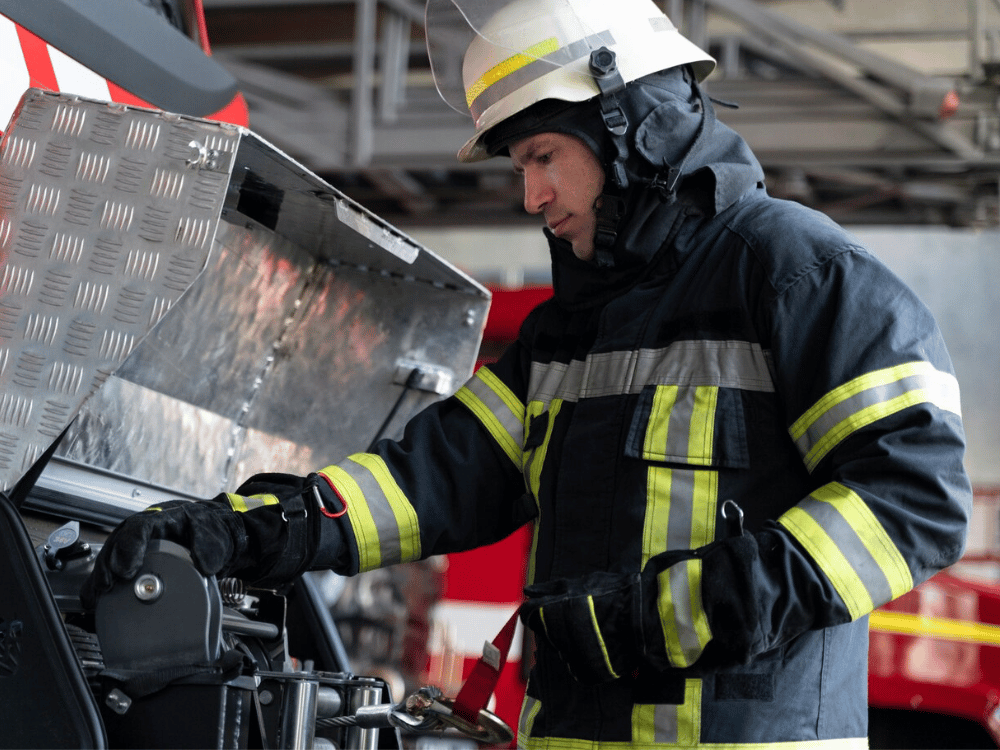 A person in a firefighter uniform is working on a fire truck.