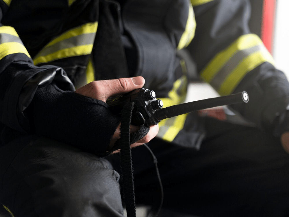 A person in a fireman's uniform is holding a radio for communication.