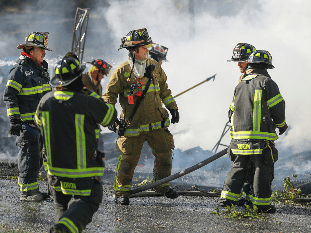 A team of firefighters in protective gear discussing at a smoky site.
