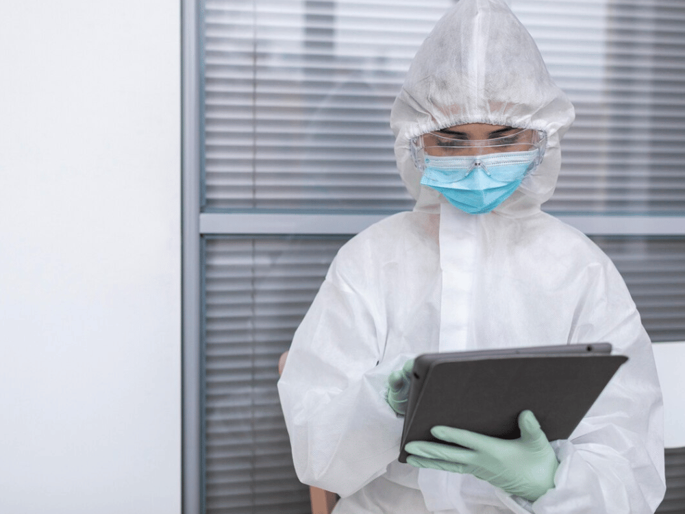 A person in a protective suit holding a tablet computer.
