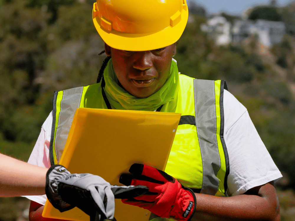 Focused construction supervisor reviewing plans on a yellow clipboard.