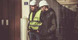 A group of workers wearing safety helmets and vests engaged in a discussion during a behavioral safety training session at a construction site.
