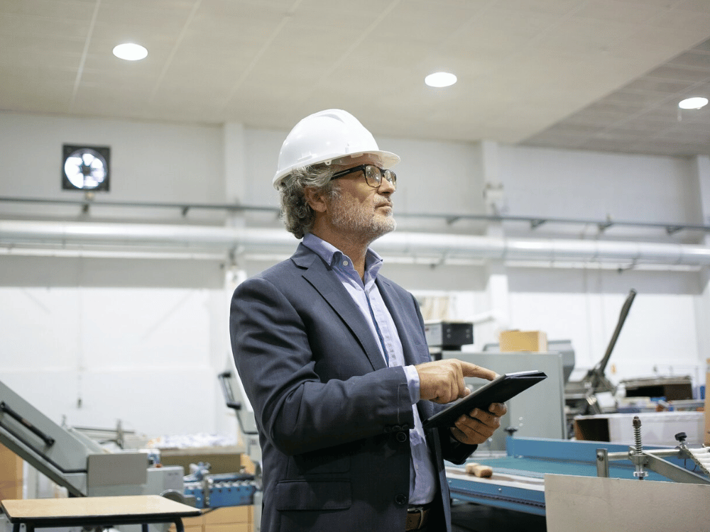 A person wearing a hard hat and glasses is standing in a factory.