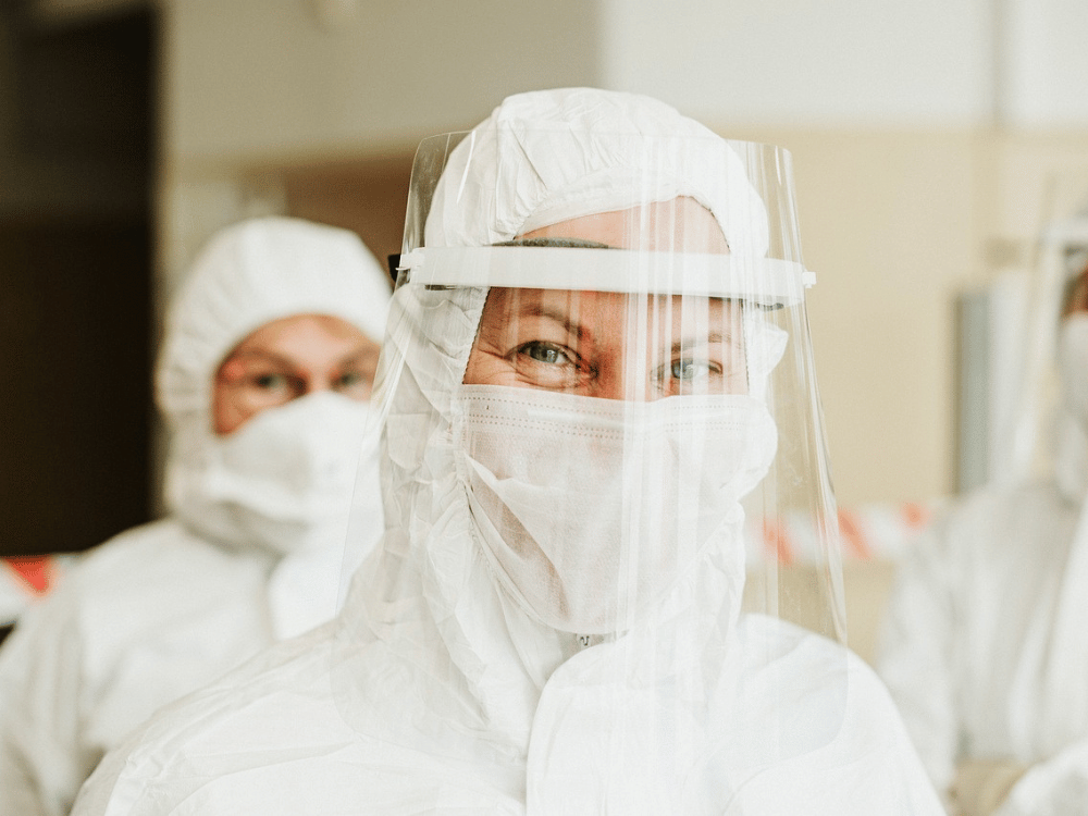 Three people in protective suits and face masks standing together.