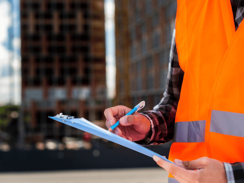 A person in an orange vest writing on a clipboard.