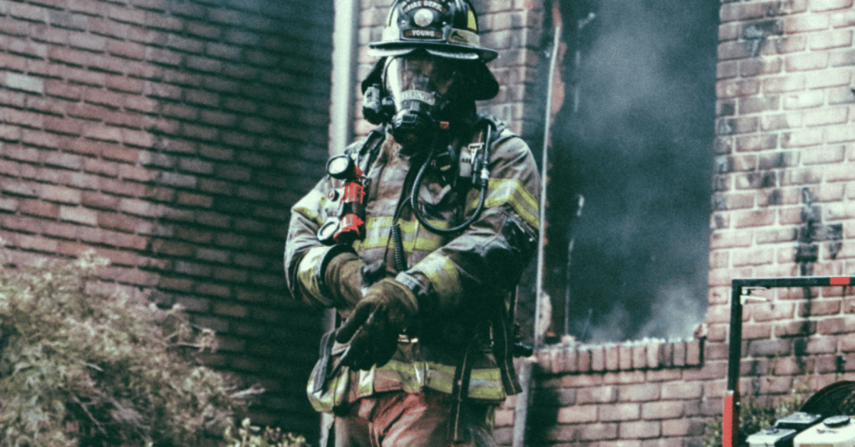 A firefighter standing in front of a building with smoke coming out of it.