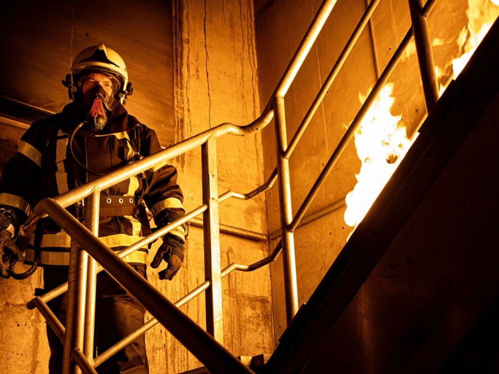 Fireman with helmet and respirator in a stairwell with visible flames.
