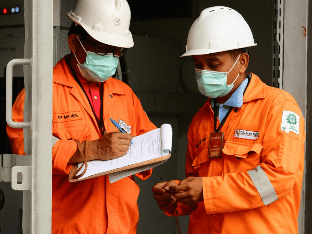 Industrial workers in orange hi-vis attire reviewing a checklist.