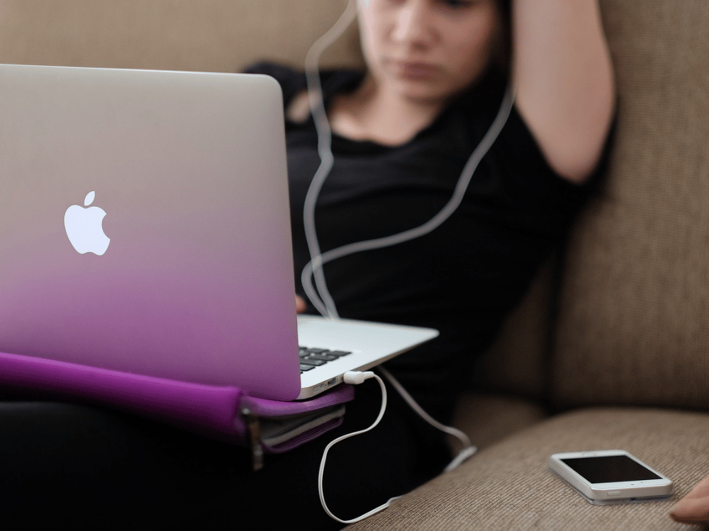 A person sitting on a couch with headphones and an apple laptop.