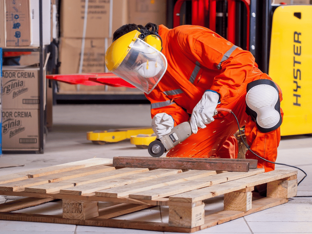 A person in an orange safety suit is working on a pallet.